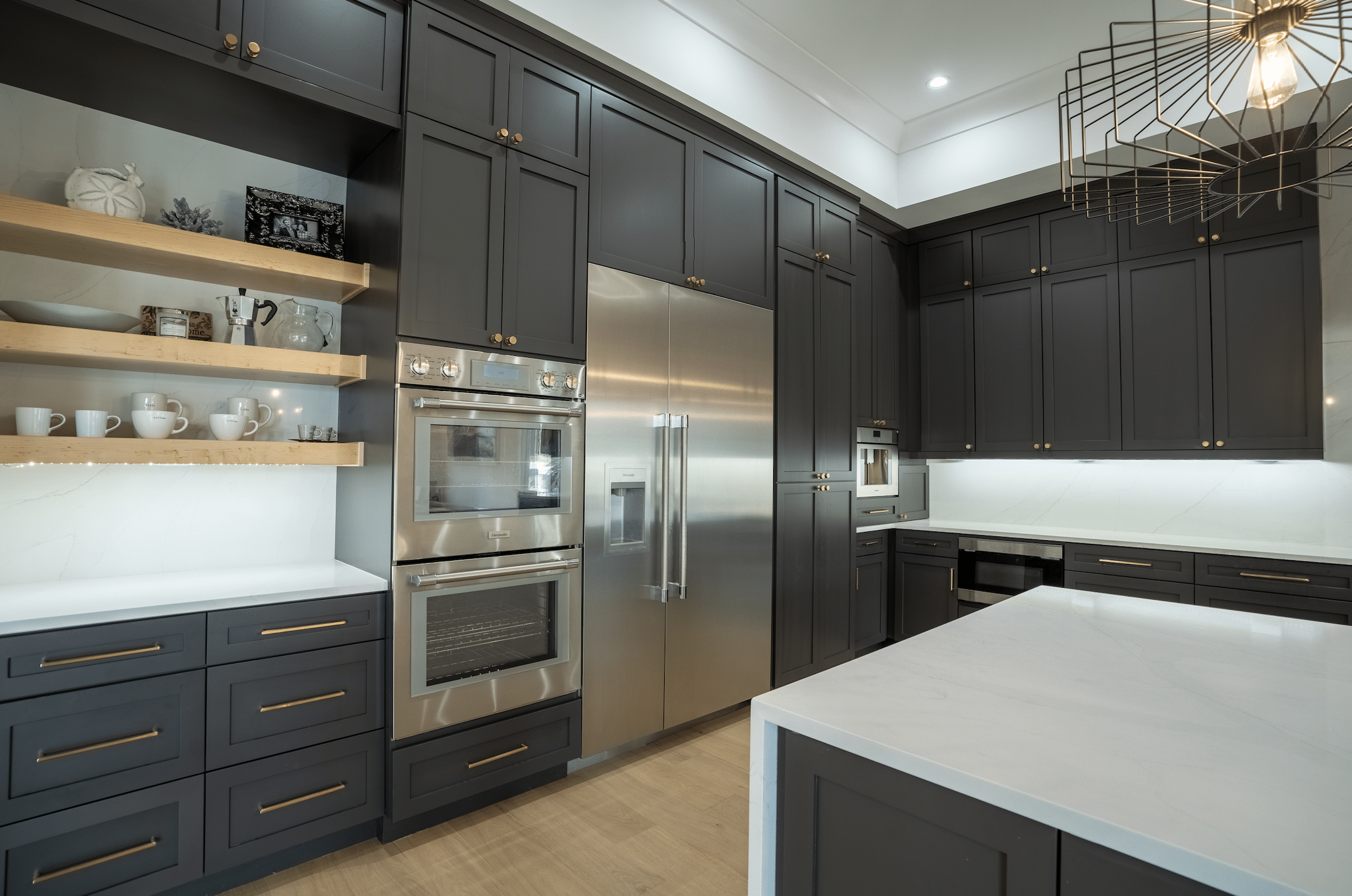 Kitchen with dark cabinetry, open shelving and stainless double ovens