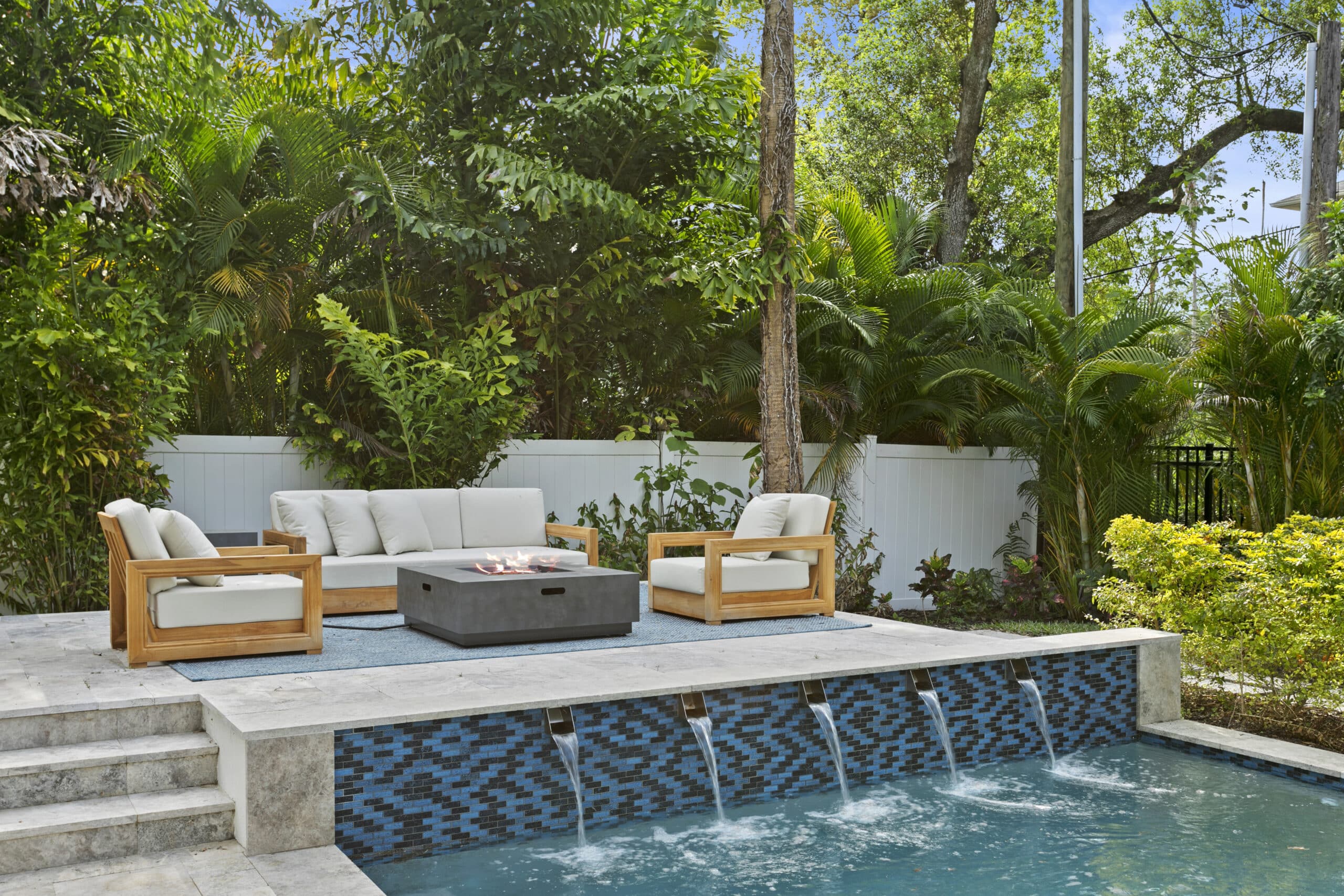 Pool with sheer water features and a fire pit lounge under mature oaks